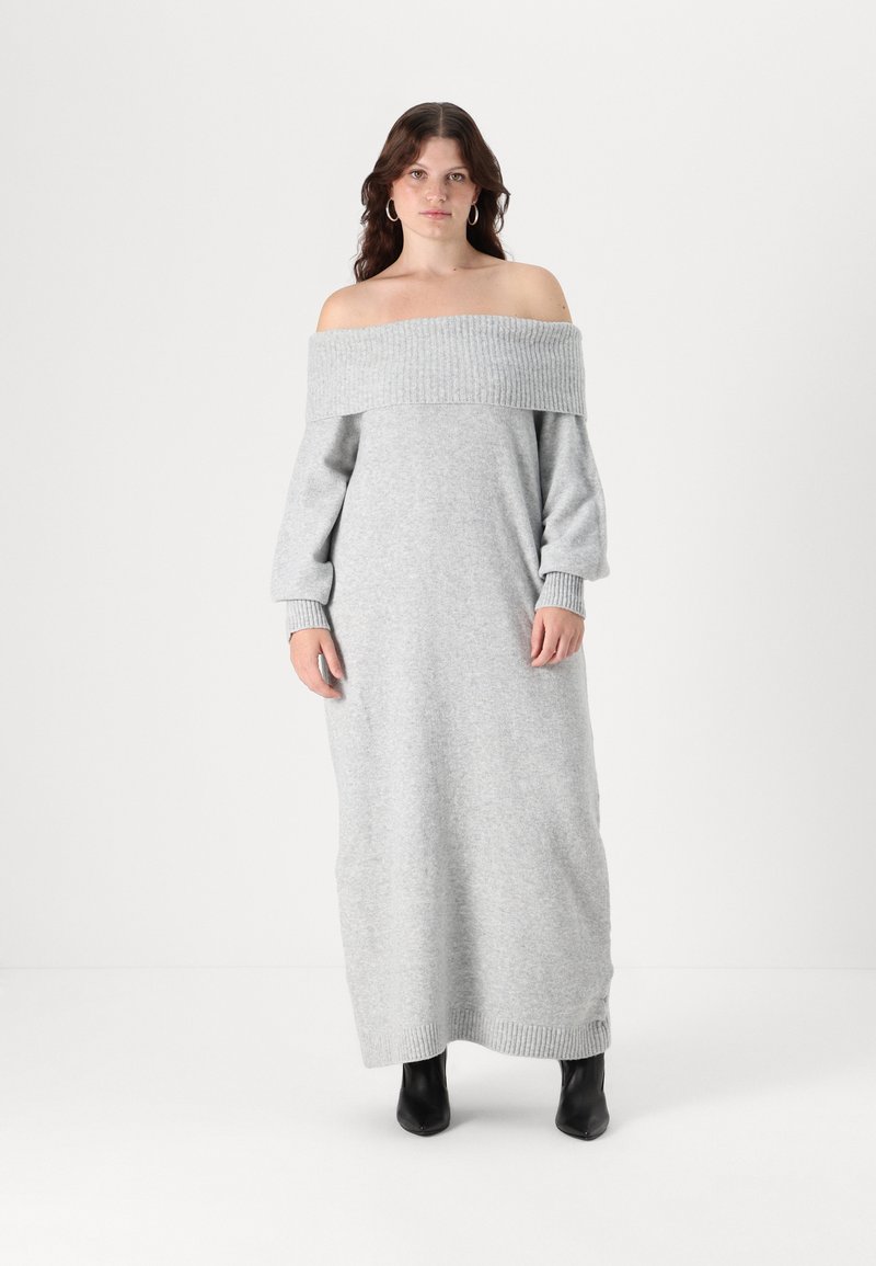 Svetlo siva off-the-shoulder pulover obleka z rebrastim izrezom in manšeti, dolgimi rokavi in ravno silhueto, v kombinaciji s črnimi gležnjarji.