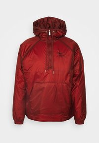 Röd huvjacka med en texturerad yta, dragsko, framficka och svart logoprydnad. Har elastiska muddar och fåll. Lättviktsmaterial.