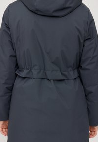 Veste matelassée longue à capuche gris foncé, cintrée à la taille. Tissu lisse et élégant, avec un design simple et sans éléments métalliques visibles.