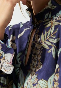 Blouse marine avec un col mao, motifs floraux en crème et sarcelle, fente au niveau du cou et tissu texturé.