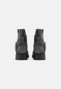 Botines de ante gris con suela negra lisa, que cuentan con una cremallera en el lateral y un detalle decorativo de borlas en el talón.
