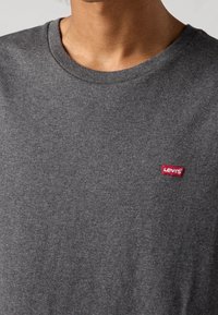 T-shirt in cotone grigio con colletto a girocollo e una piccola etichetta rossa con il logo Levis sul lato sinistro del petto. Tessuto morbido, vestibilità standard.