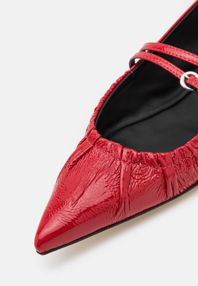 Red patent leather flat shoe with a pointed toe, gathered upper detail, and a thin ankle strap with a silver buckle.