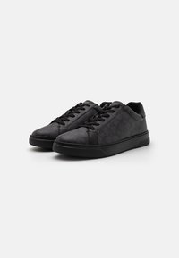 Black sneakers with a textured finish, round toe, flat black sole, and black laces. Featuring a subtle patterned design on the sides.