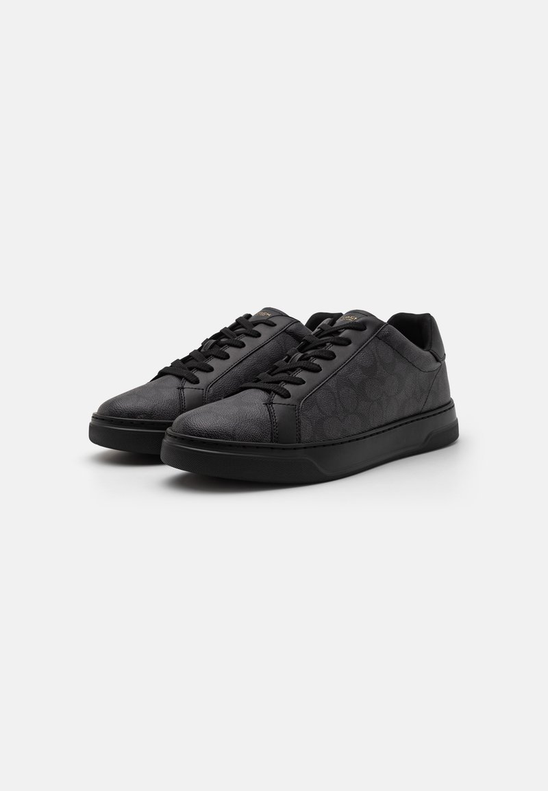 Schwarze Sneaker mit strukturierter Oberfläche, runder Zehenpartie, flacher schwarzer Sohle und schwarzen Schnürsenkeln. Mit einem dezenten Musterdesign an den Seiten.