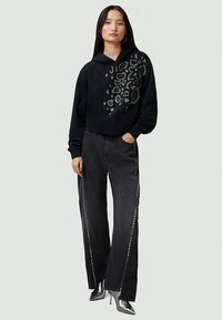 Svart kort hoodie med leopardtryck i silver rhinestones, i kombination med vida denimjeans med nitar på sidorna.