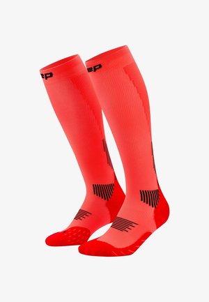 Helle, knallrote Kompressionsstrümpfe bis knapp unter das Knie mit schwarzen Akzenten an Waden, Fersen und Zehen, speziell für sportliche Aktivitäten entwickelt.