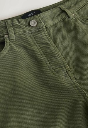 Olive green corduroy pants with a textured surface, visible stitching, front pocket, and a circular metal button. Label reads "NEXT."