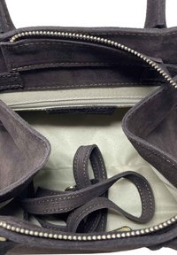 Interiér tmavě šedé semišové kabelky s několika přihrádkami, zipovou kapsou a textilní podšívkou. Obsahuje kožené popruhy a stříbrný zip.
