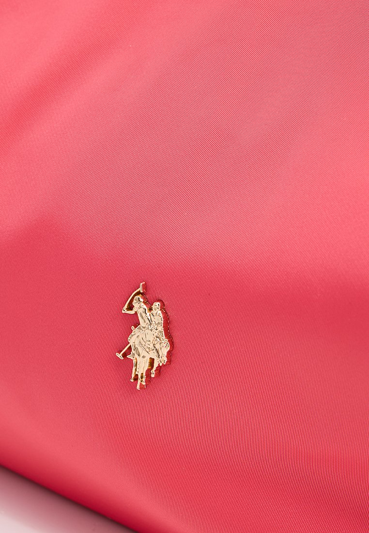 Różowa torba nylonowa o teksturowanej powierzchni, z logo złotego polo gracza jako akcentem. Prosty design, gładkie wykończenie i miękkie krawędzie.