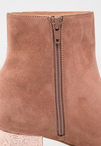 Bottine en daim marron avec fermeture éclair centrale et talon bloc texturé à finition métallique.