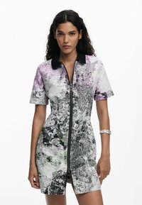 Robe à manches courtes avec une fermeture éclair à l'avant, un col noir et un motif abstrait dans les tons de violet, vert et noir sur fond blanc.