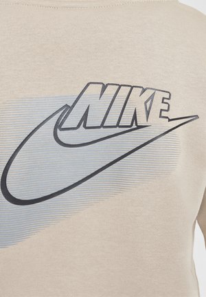 Beige huppari, jossa on suuri harmaa Nike-logo ja swoosh-suunnittelu. Pehmeä pinta, jossa on vaakasuorat raidat taustalla.