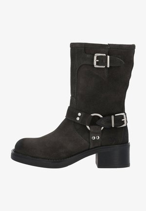 Bottine en daim noir avec un bout rond, une boucle sur le côté et des sangles décoratives. Elle dispose d'un petit talon bloc et d'une semelle en caoutchouc texturé.