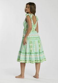 Vestido de patrón verde y azul claro con escote en V, falda acampanada de volantes y tirantes con lazo. Tejido de algodón con diseños geométricos.