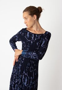 Robe longue à manches longues de couleur marine avec des motifs floraux en bleu clair, dotée d'un décolleté carré et d'une texture côtelée. Les accents comprennent des poignets bleus.