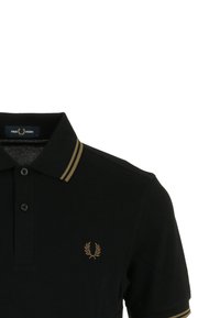 Polo negro de Fred Perry con doble franja beige en el cuello y la manga, dos botones y logo de laurel beige en el pecho.