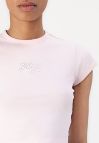 Rožinė medvilninė marškinė su trumpomis rankovėmis, su apvalia iškirpte ir blizgančiu "Hugs" grafiniu dizainu krūtinėje, puoštu rhinestones.