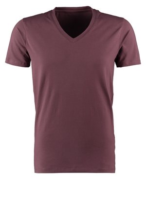 Man loopt, draagt een paars T-shirt, grijze spijkerbroek, witte sneakers, een geruite sjaal en een beige armband om zijn linkerpols.