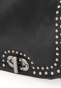 Sac en cuir noir avec des accents métalliques. Présente un fermoir argenté et des clous le long du bord pour un rendu texturé supplémentaire.