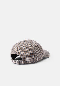 Barna, kék és krém színű houndstooth mintás sapka, ívelt billentéssel, állítható hátsó pánttal és texturált anyaggal.