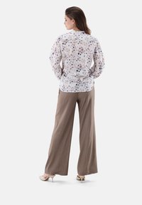 Floral-patterned blouse in light fabric with long sleeves, paired with beige wide-leg trousers and cream heels. Viewed from the back.