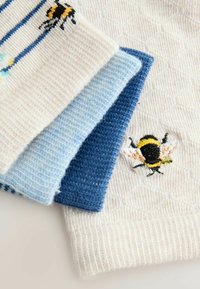 Gebreide sokken in beige, lichtblauw en donkerblauw met een honingraatstructuur. Bijenborduurwerk op de beige sok; gestreept patroon op de lichtblauwe sok.