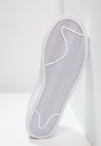 Suela de zapatilla blanca con un patrón de tracción en espiga, que presenta una textura de goma suave y una forma curva, reposando sobre un fondo claro.