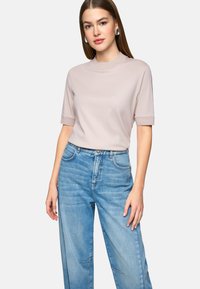 Hellrosa Kurzarmoberteil mit hohem Kragen, kombiniert mit locker sitzenden blauen Jeans. Der Stoff wirkt weich und glatt.