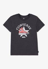 Tamsiai pilka medvilninė marškinėliai su raudonos Converse sportbačio su baltais akcentais grafika ir tekstu virš jo, išdėstytu ant žvaigždės.