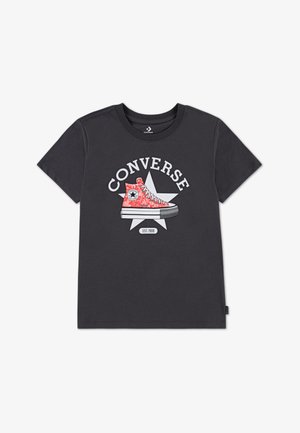 Maglietta di cotone grigio scuro con una grafica di una sneaker Converse rossa con dettagli bianchi e testo sopra, mostrata su una stella.