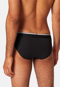 Schwarze Baumwollunterhose mit tiefem Schnitt, ausgestattet mit einem schmalen elastischen Bund mit einem dezenten grauen Streifen. Strukturierte, glatte Oberfläche.