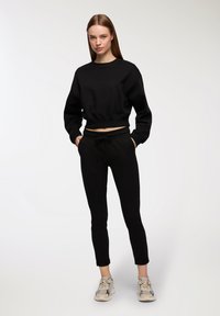 Felpa nera corta con scollatura tonda e maniche lunghe, abbinata a pantaloni jogger neri con elastico in vita e tasche laterali.