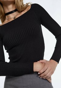 Schwarzes, geripptes, schulterfreies Oberteil mit langen Ärmeln, das über eine glatte Textur und eine taillierte Passform verfügt, kombiniert mit einem grauen Rock.