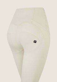 Leggings bianchi a vita alta con una texture liscia, caratterizzati da cuciture curve, doppi tasche e un piccolo dettaglio del logo nero sul lato.