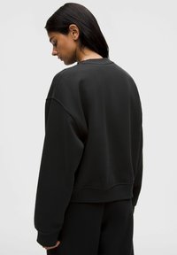 Schwarzer übergroßer Pullover, Baumwollmischung, runder Halsausschnitt, gesenkte Schulternähte, gerippte Bündchen und Saum. Glatte Textur ohne Muster.