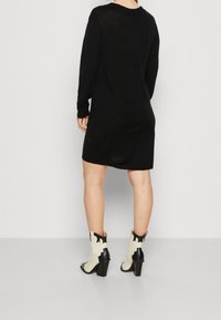 Abito a maglia lungo nero con maniche lunghe e vestibilità rilassata, caratterizzato da un collo tondo, abbinato a stivali alla caviglia con tacco bianchi e neri.