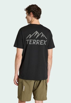 Mann von hinten, trägt ein schwarzes Terrex T-Shirt mit Berglogo und olivgrüne Shorts mit Terrex-Logo an der Seitentasche.