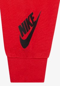 Crvene pamučne trenirke s crnim Nike logotipom otisnutim na lijevom bedru i rebrastim rubom na gležnju. Mekana tekstura s brušenim završetkom.
