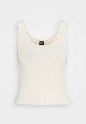 Débardeur côtelé blanc cassé avec bordure en dentelle le long du col et des emmanchures. Tissu doux, coupe ajustée et encolure ronde. Étiquette à l'intérieur du col.