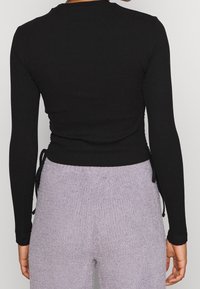Svart ribbad långärmad topp med justerbara sidoknutar, med en åtsittande design och rund halsringning, matchad med ljuslila texturerade byxor.