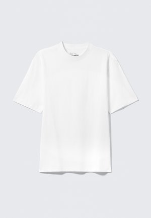 Cămașă T-shirt albă, cu mâneci scurte, de tip relaxat, așezată pe un fundal gri deschis.