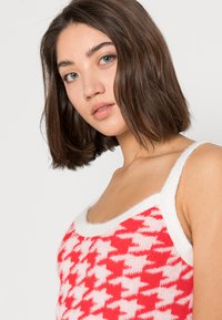 Top de malha com padrão quadriculado em vermelho e branco, com uma textura suave e um acabamento branco ao longo do decote e das alças.