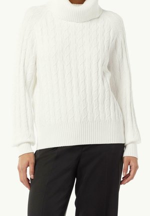 Pull à col roulé blanc en maille torsadée porté avec un pantalon noir, montrant des poignets et un ourlet côtelés, mains détendues le long du corps.