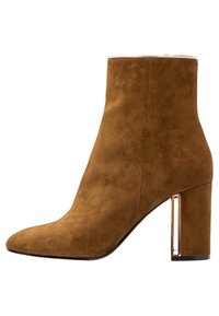 Bottine en daim brun avec un bout pointu, talon bloc haut avec un accent doré, texture lisse et silhouette élégante.