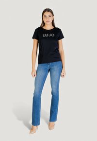 T-shirt en coton noir avec un logo argenté "LIU•JO" sur le devant, associée à un jean en denim bleu et des escarpins nude.