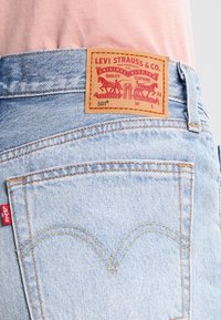 Světle modré džíny z denimu s hnědou koženou etiketou s nápisem "Levi Strauss & Co" a červeným štítkem na boku. Klasický design s pěti kapsami.