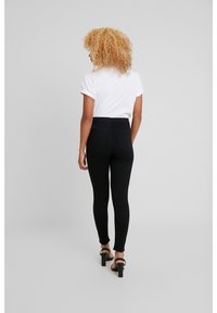 Černé legíny s vysokým pasem a hladkou texturou, které mají dvě zadní kapsy a přiléhavý střih, v kombinaci s bílým tričkem s ohrnutými rukávy.