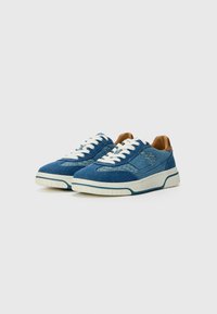 Baskets en denim bleu avec des lacets blancs, semelle en caoutchouc crème et accents en cuir brun au talon. Présente un design texturé sur les côtés.