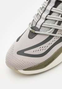 Jasnoszary but sportowy z oddychającą cholewką z siateczki, teksturowanymi detalami i ciemnoszarymi akcentami. Posiada amortyzowaną podeszwę oznaczoną "ADIPRENE+".